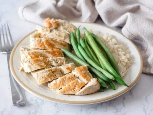 chicken sliced on a plate, with green beans and rice.