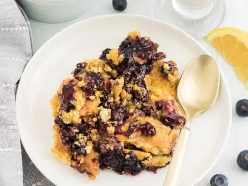 lemon blueberry dump cake on a plate, with glass of milk and bowl of blueberries.