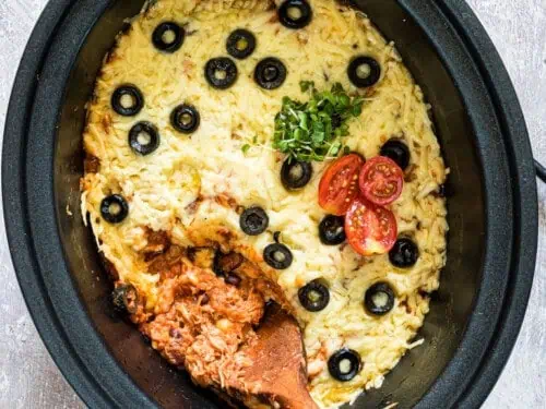 chicken enchilada casserole in a crock pot, topped with cheese, olives, and tomatoes.