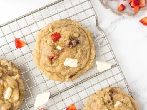 strawberry cookies covered in white chocolate chunks on a baking rack.