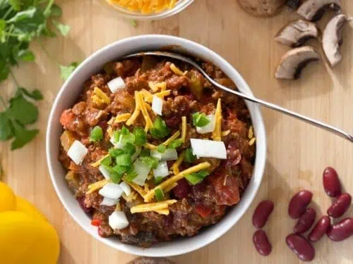 bowl of chili topped with onions, cheese.