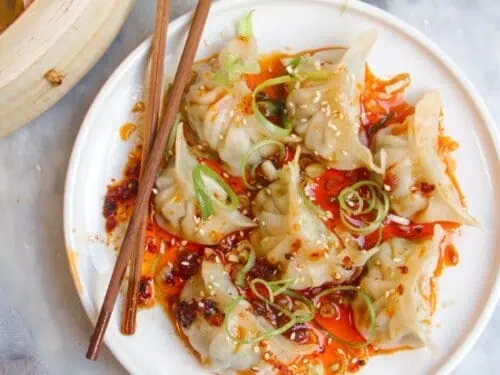 pork dumplings covered in sauce on a plate, with chopsticks.
