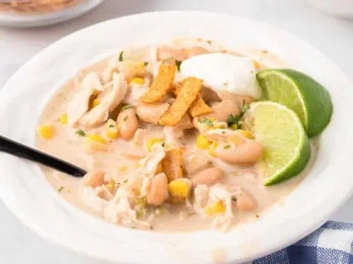 bowl of white chicken chili with a spoon in it, topped with lime and sour cream.