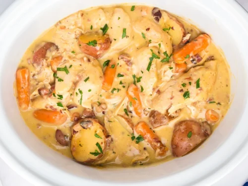 chicken, potatoes, and carrots in a creamy sauce in a crock pot.
