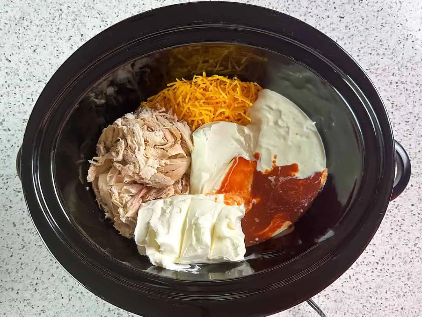 ingredients for buffalo chicken dip in a crock pot.