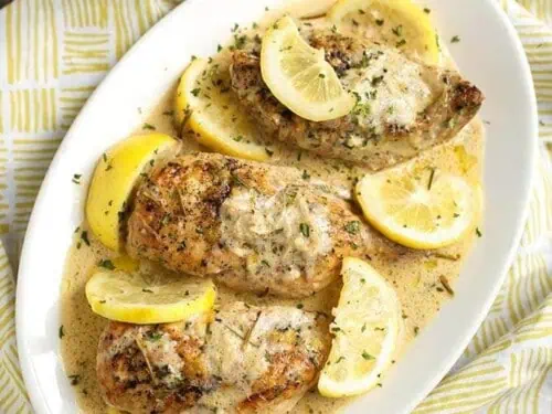 chicken breasts on a platter, covered in a creamy sauce and lemon slices.