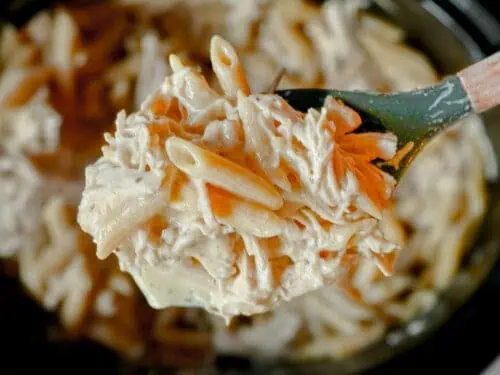 spoonful of crockpot olive garden chicken pasta held above a slow cooker.