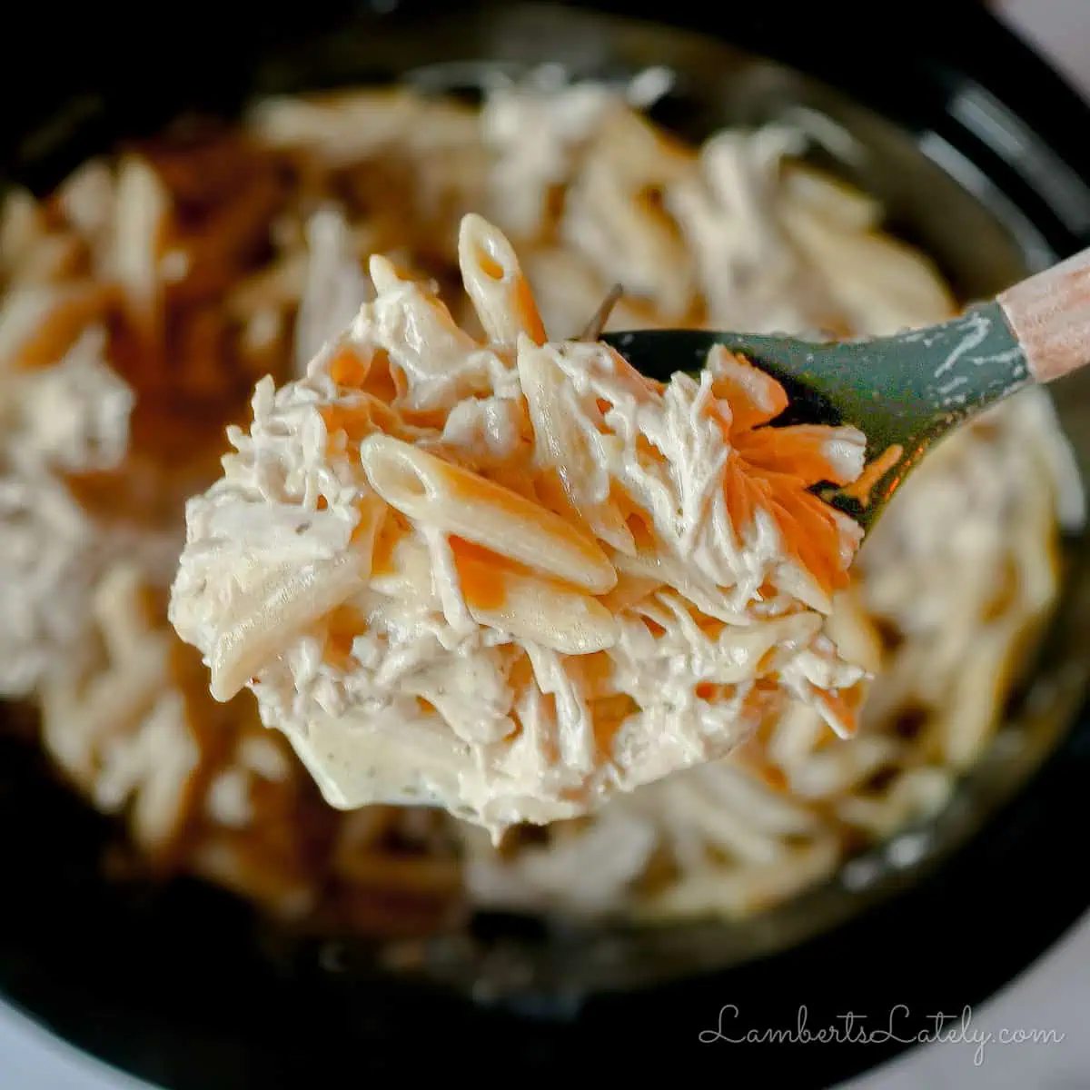 spoonful of crockpot olive garden chicken pasta held above a slow cooker.