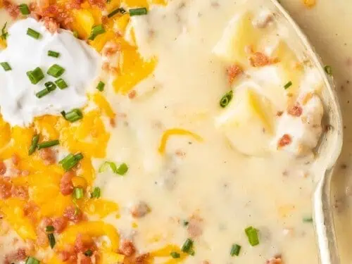 dipping a spoon into a bowl of sausage potato soup.