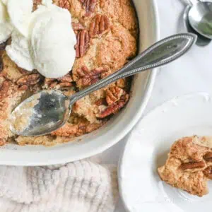 pecan cobbler in a casserole dish, with spoon, topped with ice cream.