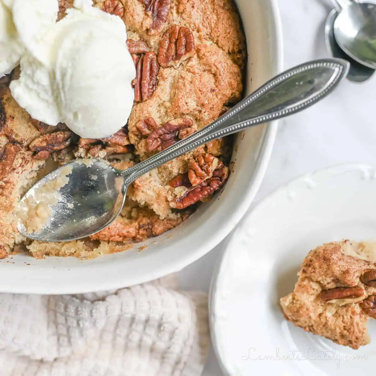 pecan cobbler in a casserole dish, with spoon, topped with ice cream.