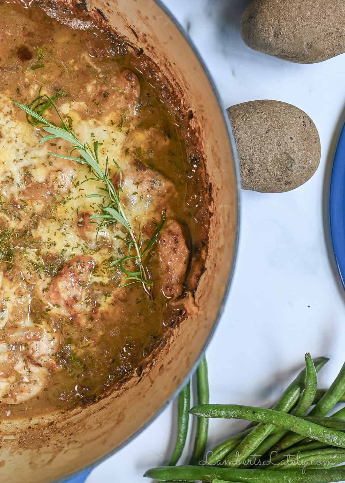 french onion chicken bake in a cast iron pan, with green beans and potatoes next to it.