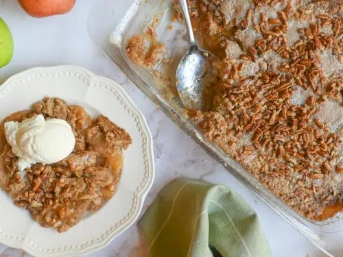 caramel apple dump cake in a baking dish, with serving topped with ice cream next to it.