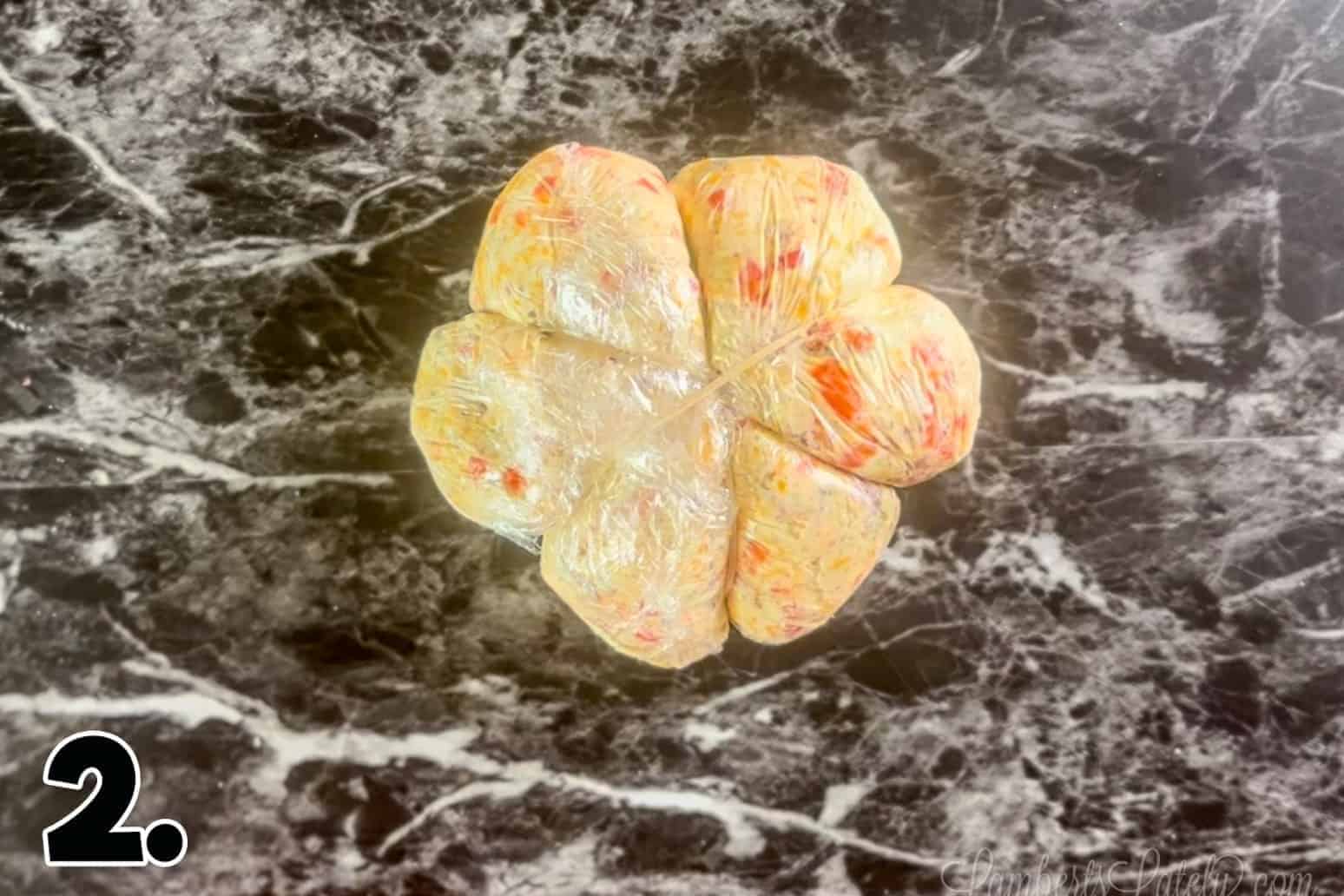 cheese ball wrapped in plastic wrap and rubber bands.