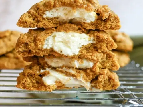 stack of pumpkin cheesecake cookies cut in half, showing cream cheese filling.