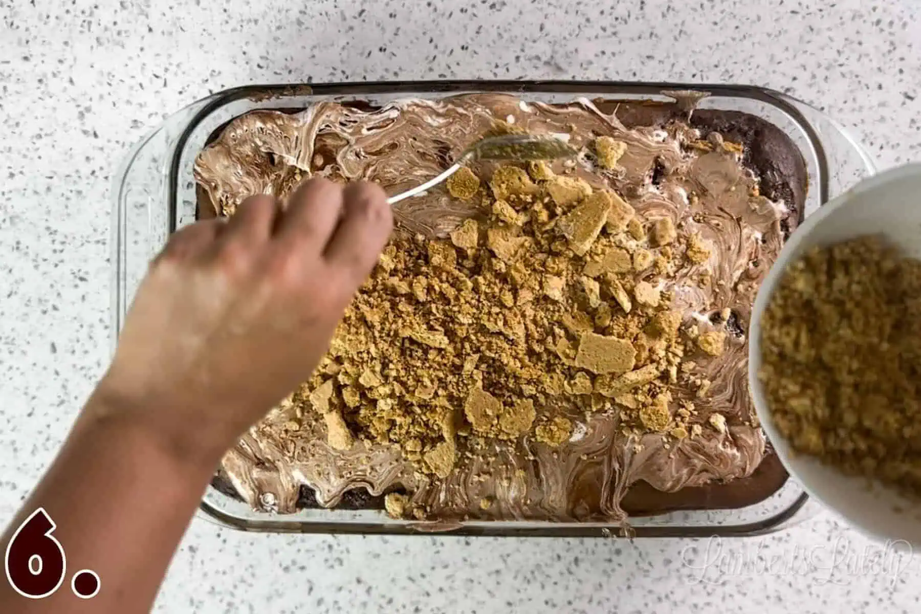 spreading graham cracker crumble on top of the cake.