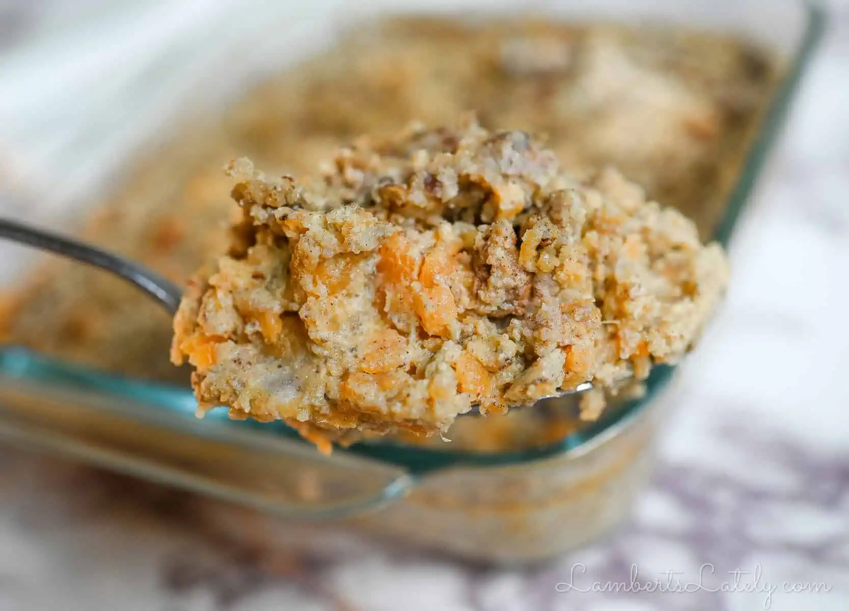 holding a spoonful of sweet potatoes in front of a casserole dish.