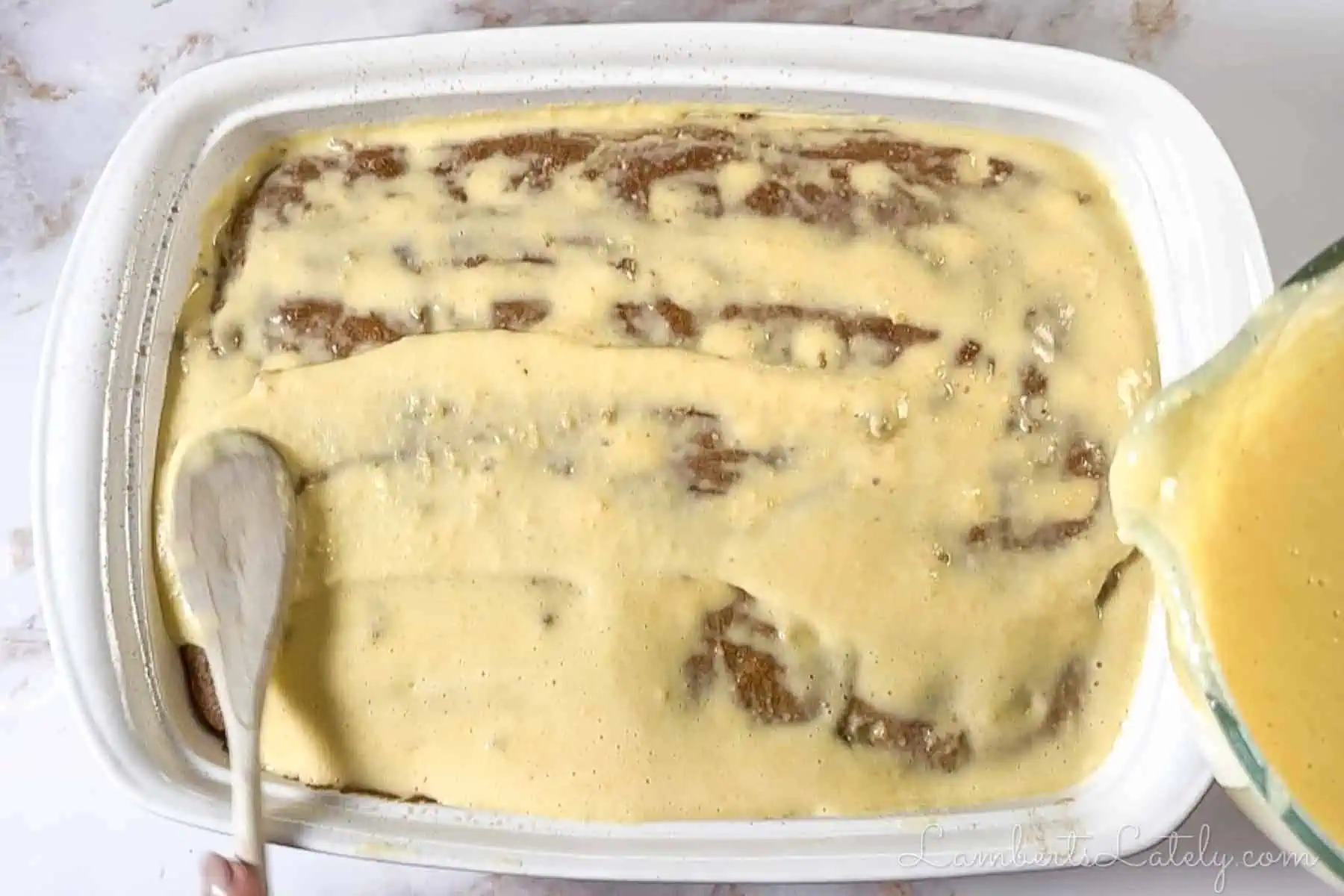 pouring eggnog pudding mixture over the cake with holes.