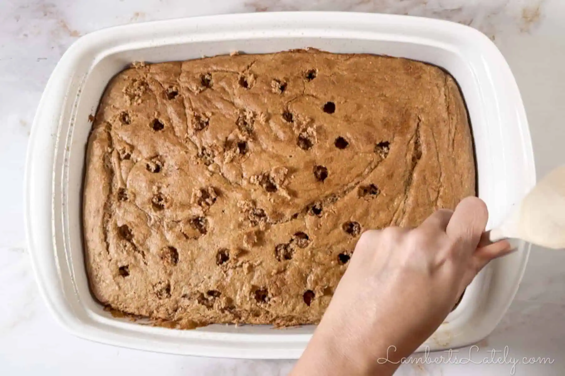 poking holes in a baked spice cake with the back of a wooden spoon.