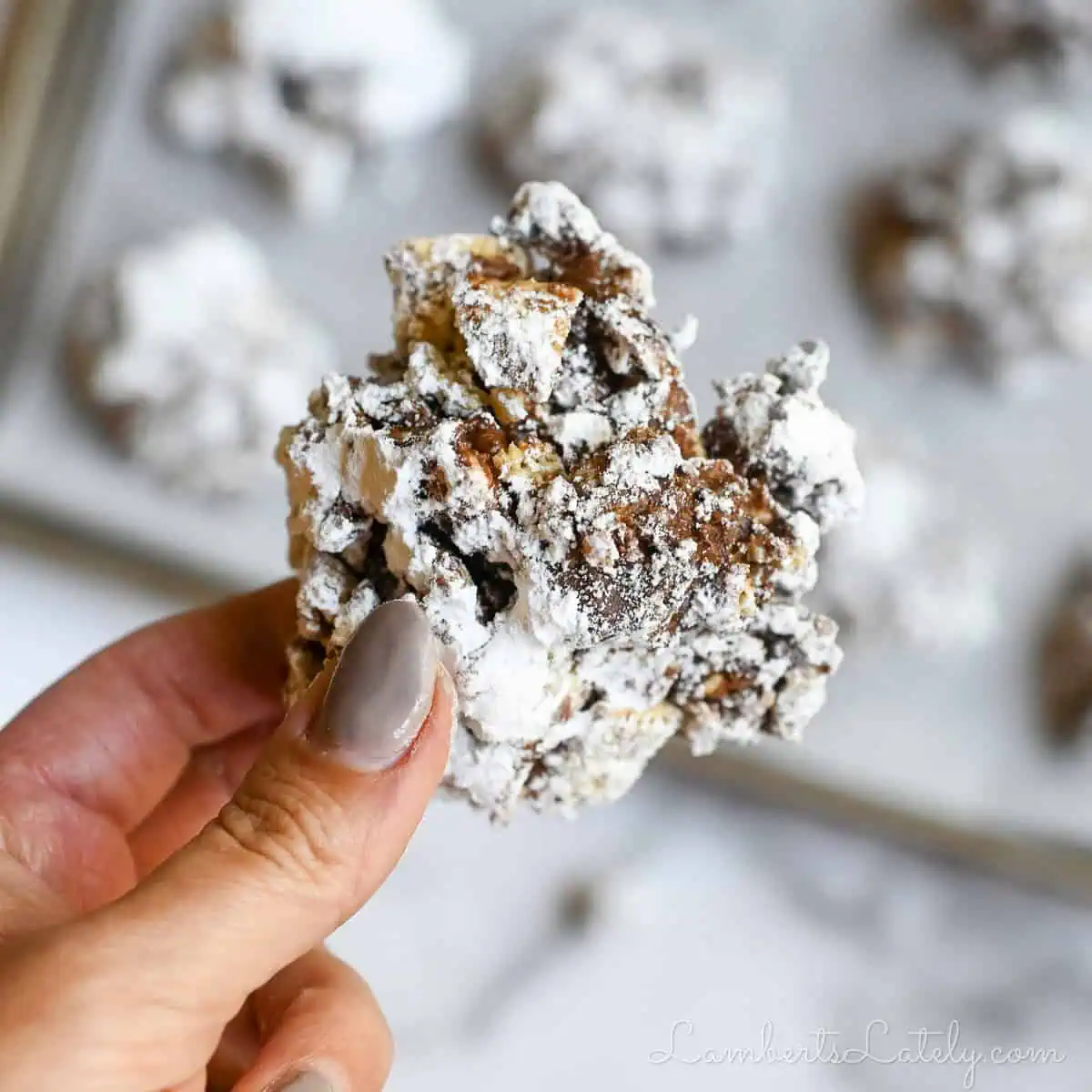 holding a muddy buddies cookie in front of a baking sheet full of cookies.