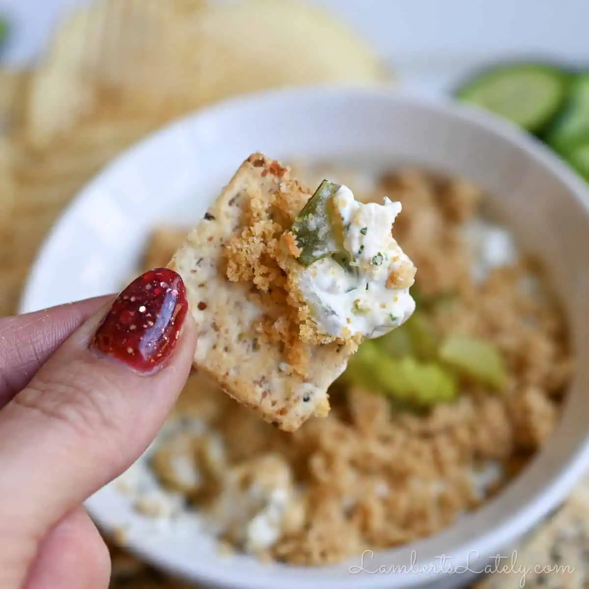 holding fried pickle dip on a cracker.