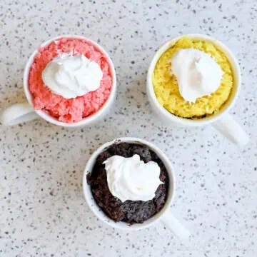 3 mug cakes; strawberry, chocolate, and lemon; covered in whipped cream.