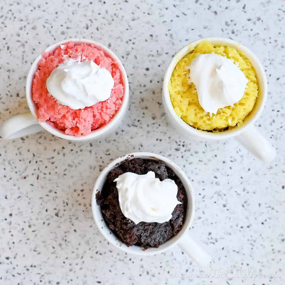 3 mug cakes; strawberry, chocolate, and lemon; covered in whipped cream.