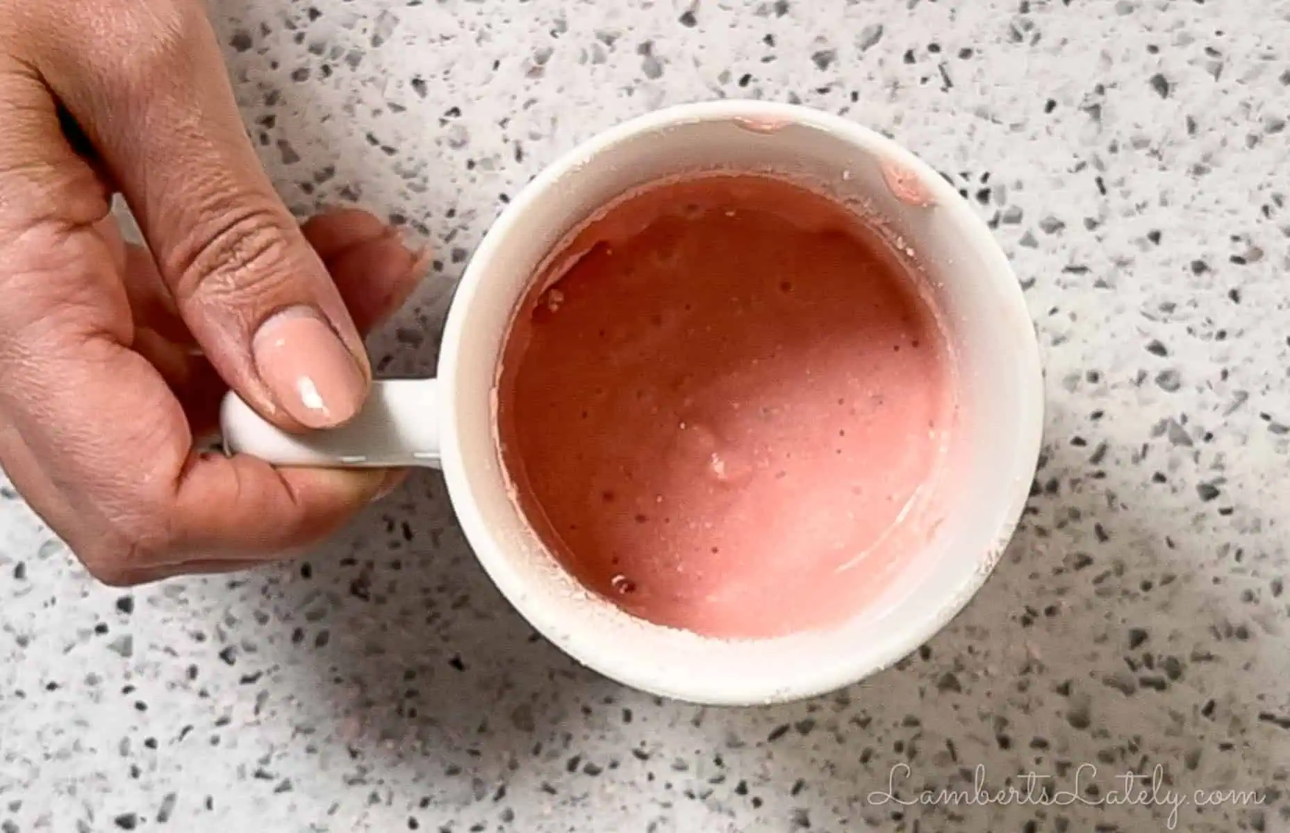 holding a mug full of strawberry cake batter.