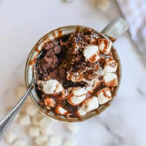 hot chocolate mug cake covered in marshmallows and chocolate syrup.