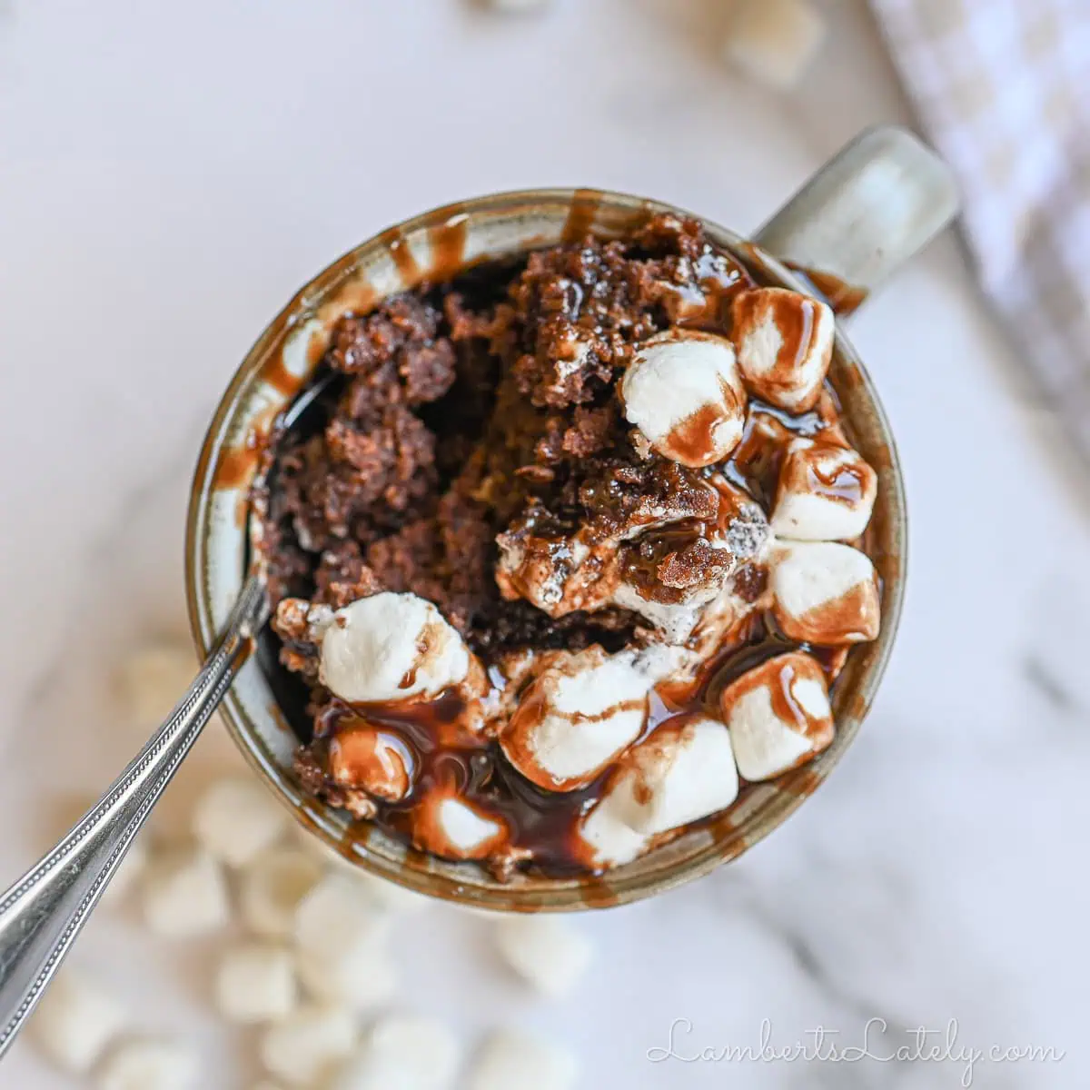 hot chocolate mug cake covered in marshmallows and chocolate syrup.