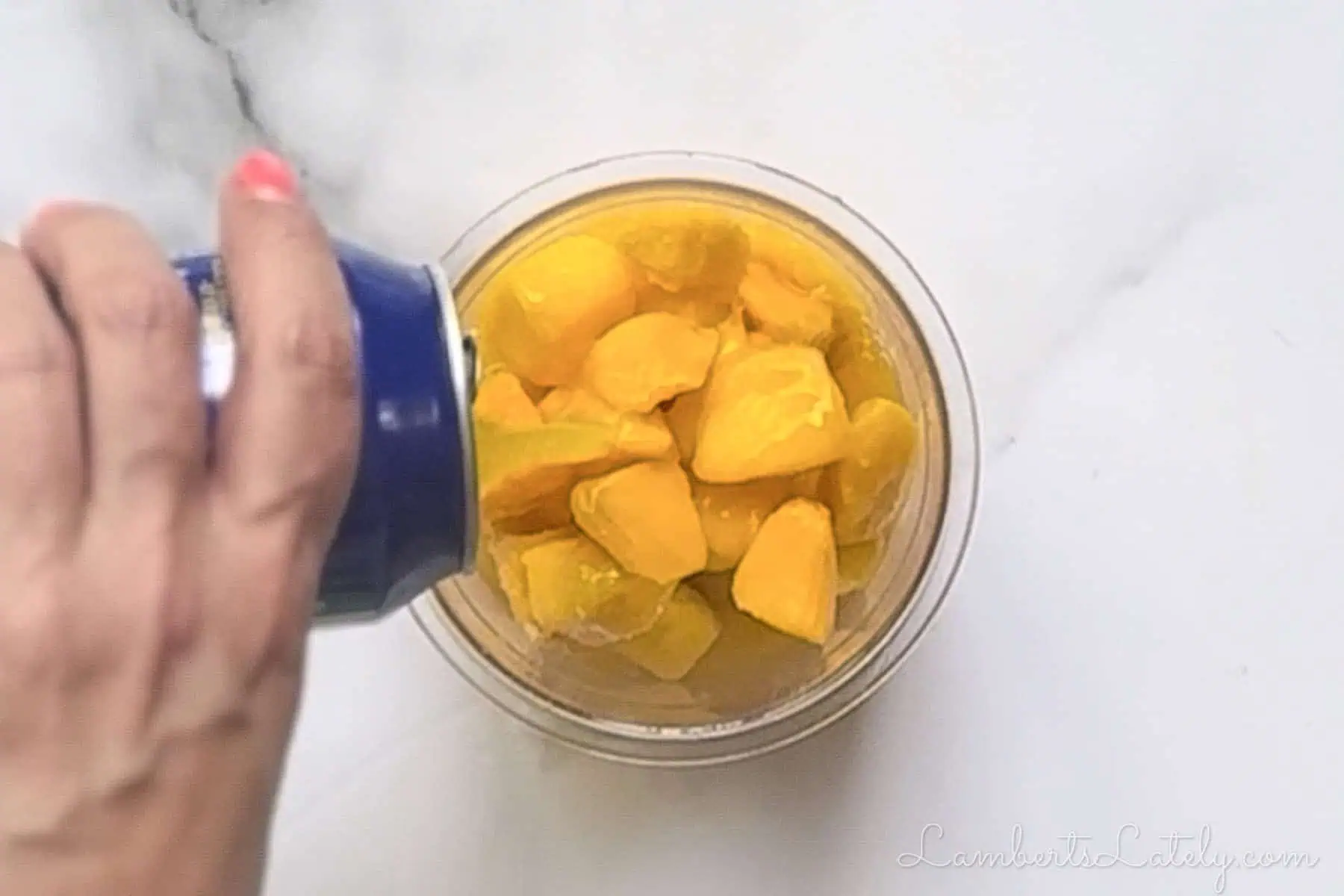 pouring mango nectar into a ninja creami bowl of frozen mango.
