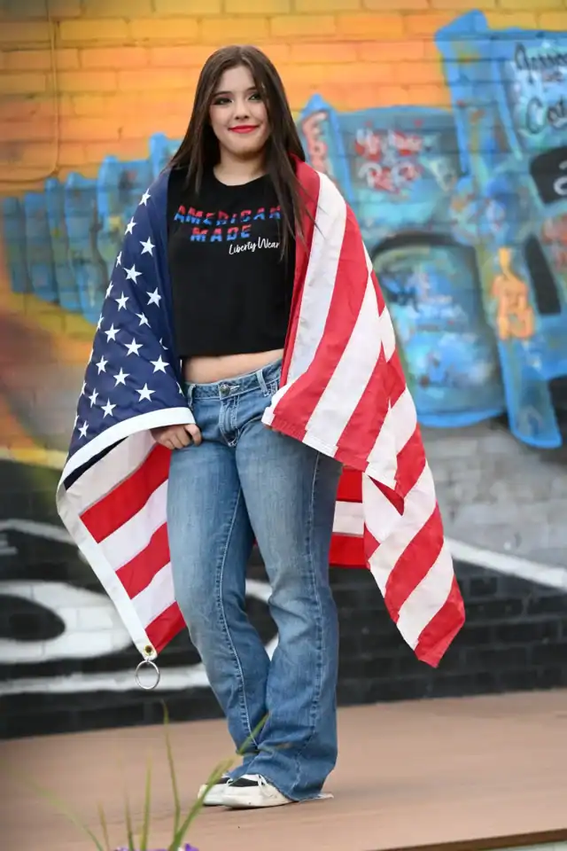 A woman in jeans and a black Liberty Wear t-shirt holding an American flag