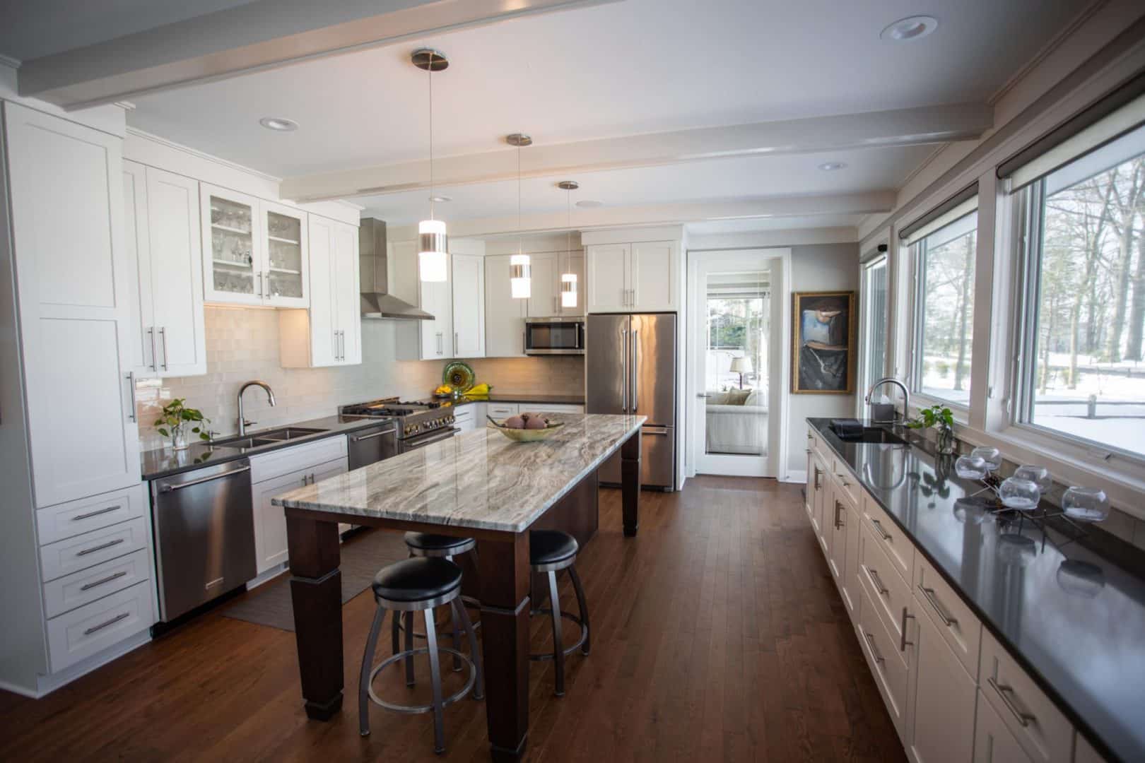 Modern kitchen with white cabinetry, granite countertops, and ample natural light from large windows.