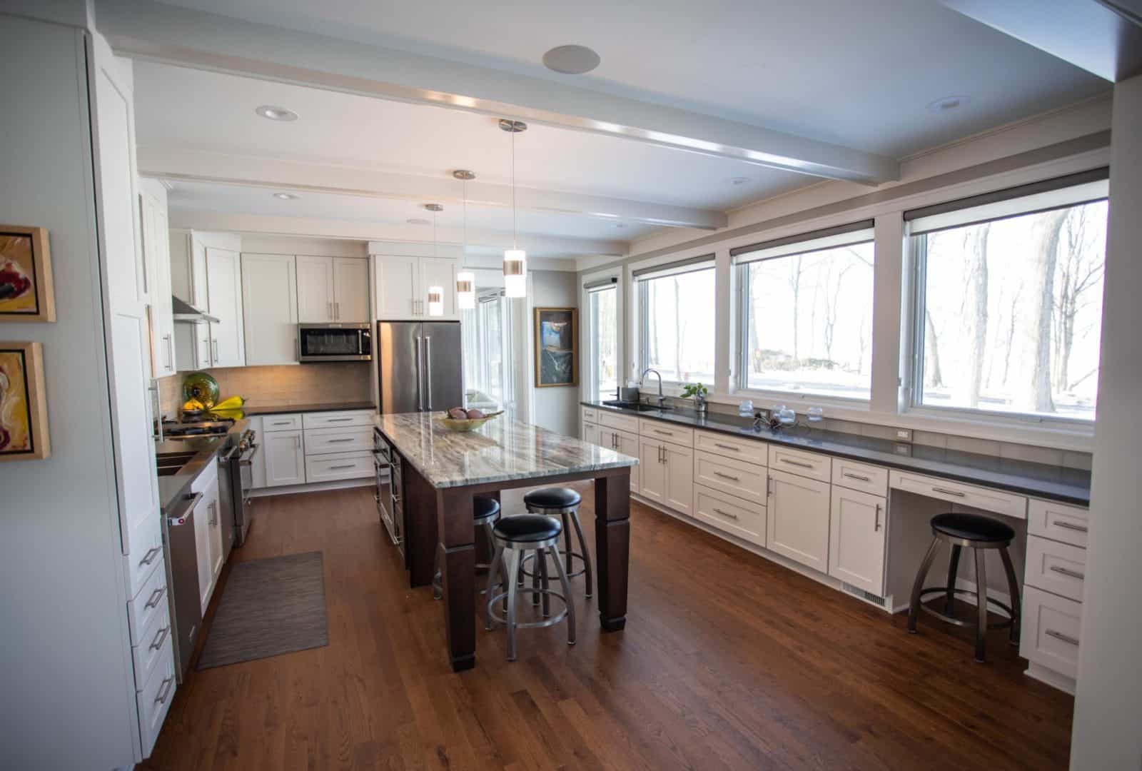 Spacious kitchen featuring large windows, white cabinetry, and a central island with seating. Perfec.