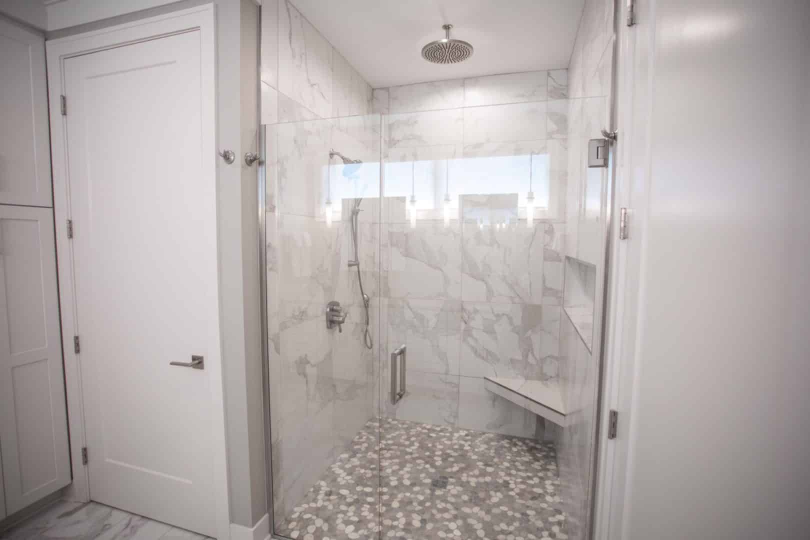 Modern marble walk-in shower with glass door and built-in bench.