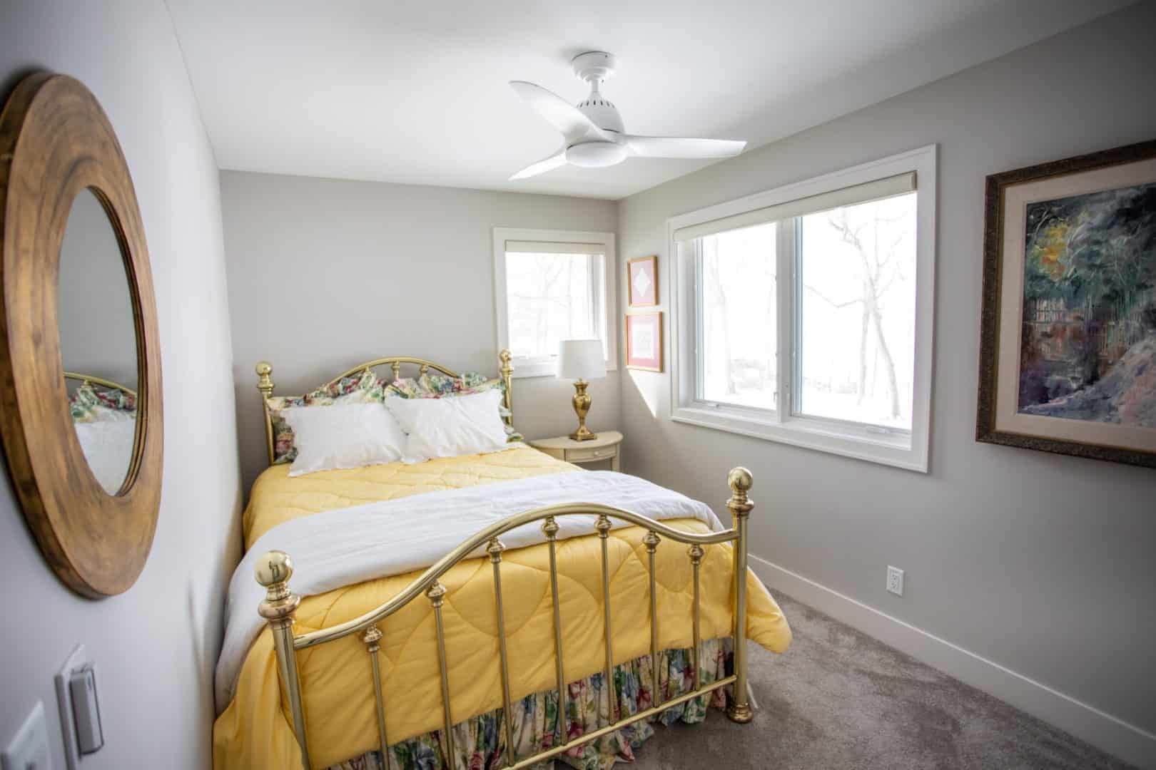 Bright bedroom with a gold metal bed frame and yellow bedding, featuring large windows and modern de.