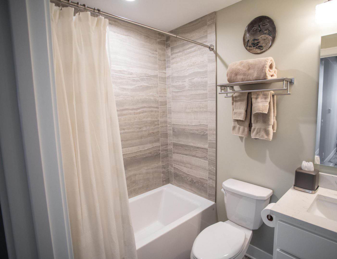 Bathroom with bathtub, shower curtain, and beige towels in a contemporary home.