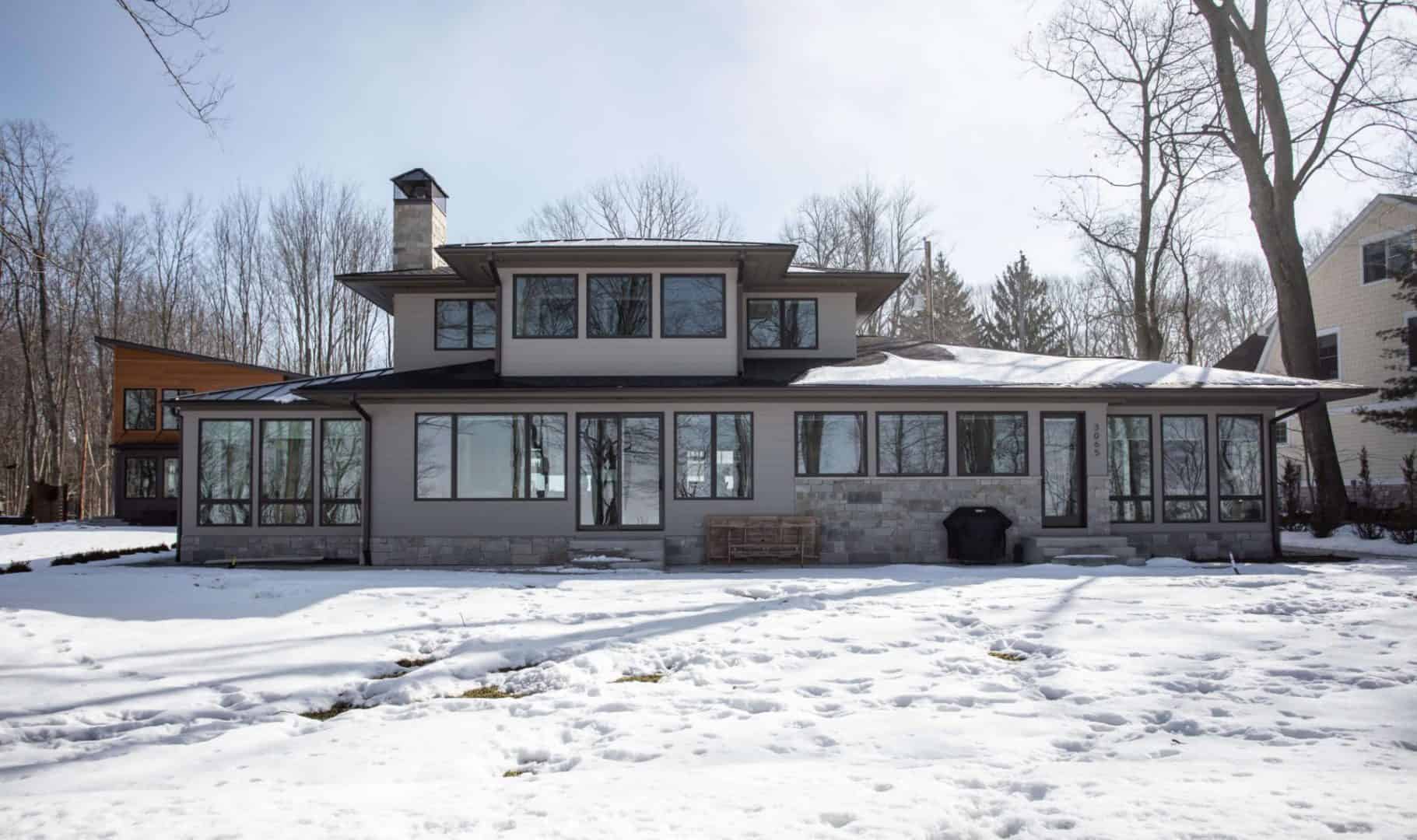Modern lakefront house with large windows and spacious porch during winter.