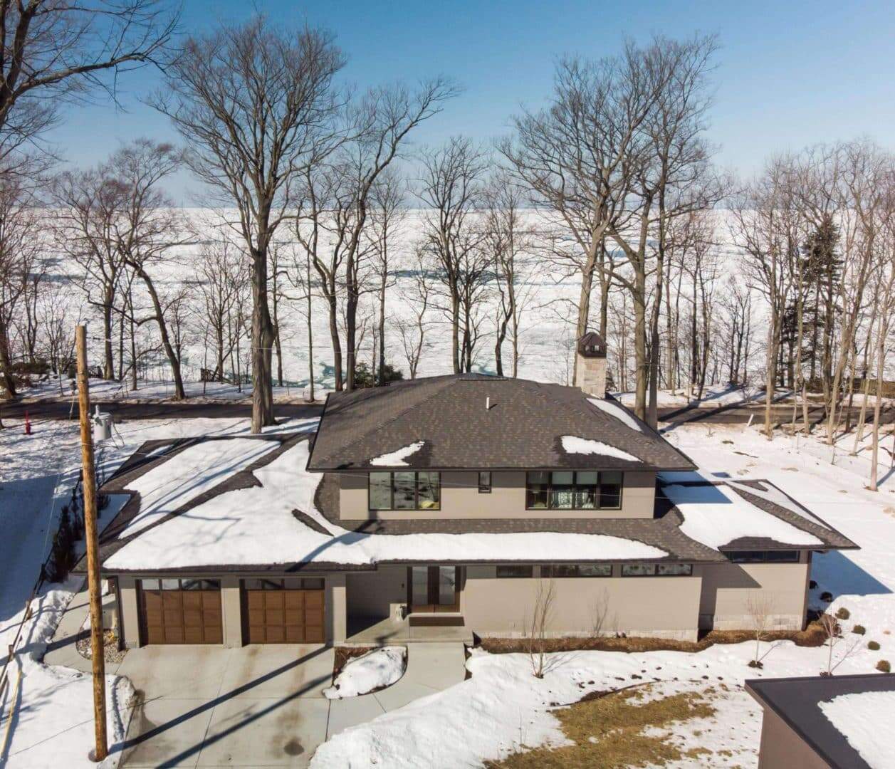 Modern winter home with snow-covered roof and surrounding trees.