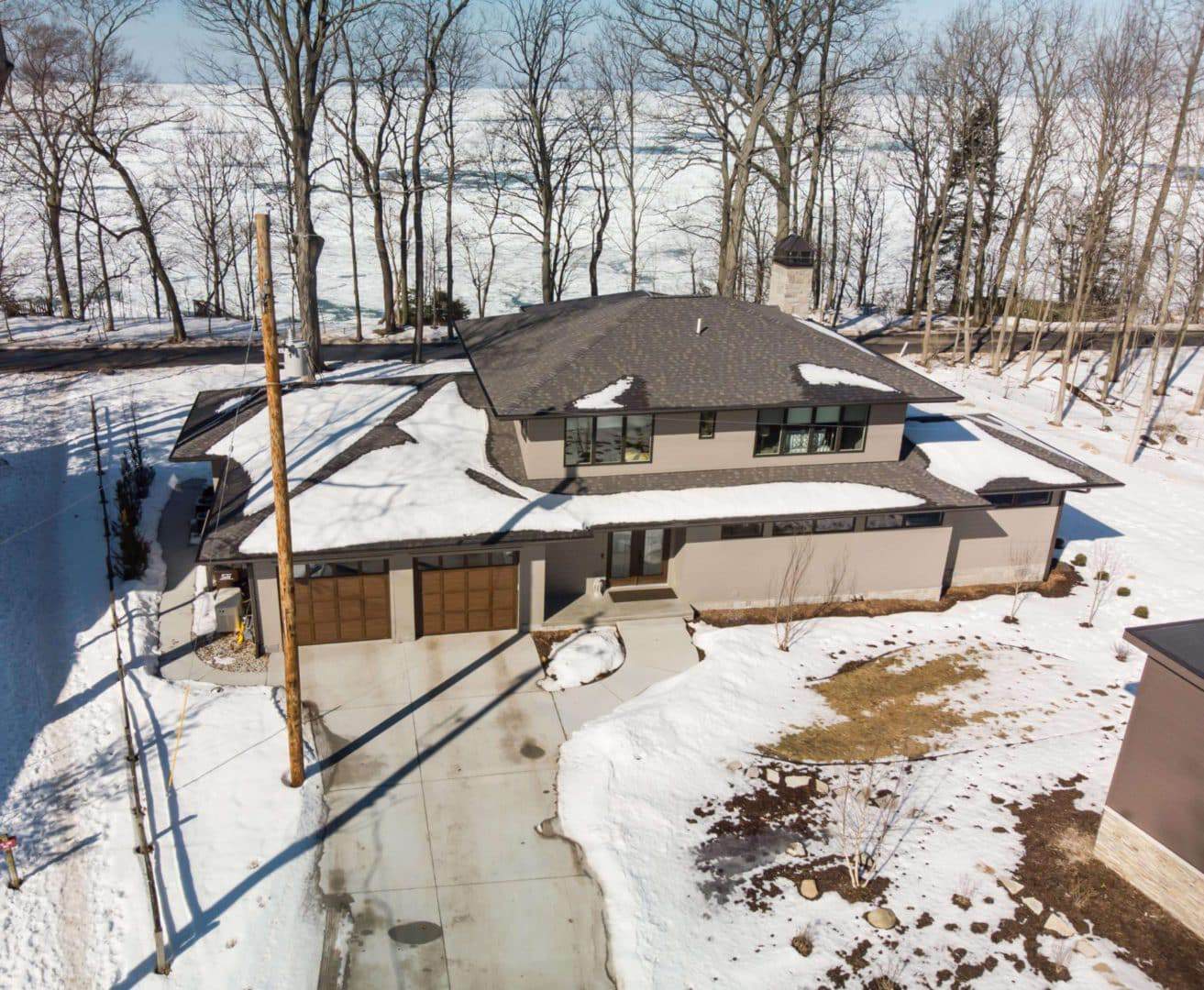 Modern house with snow-covered roof and driveway in a winter setting.