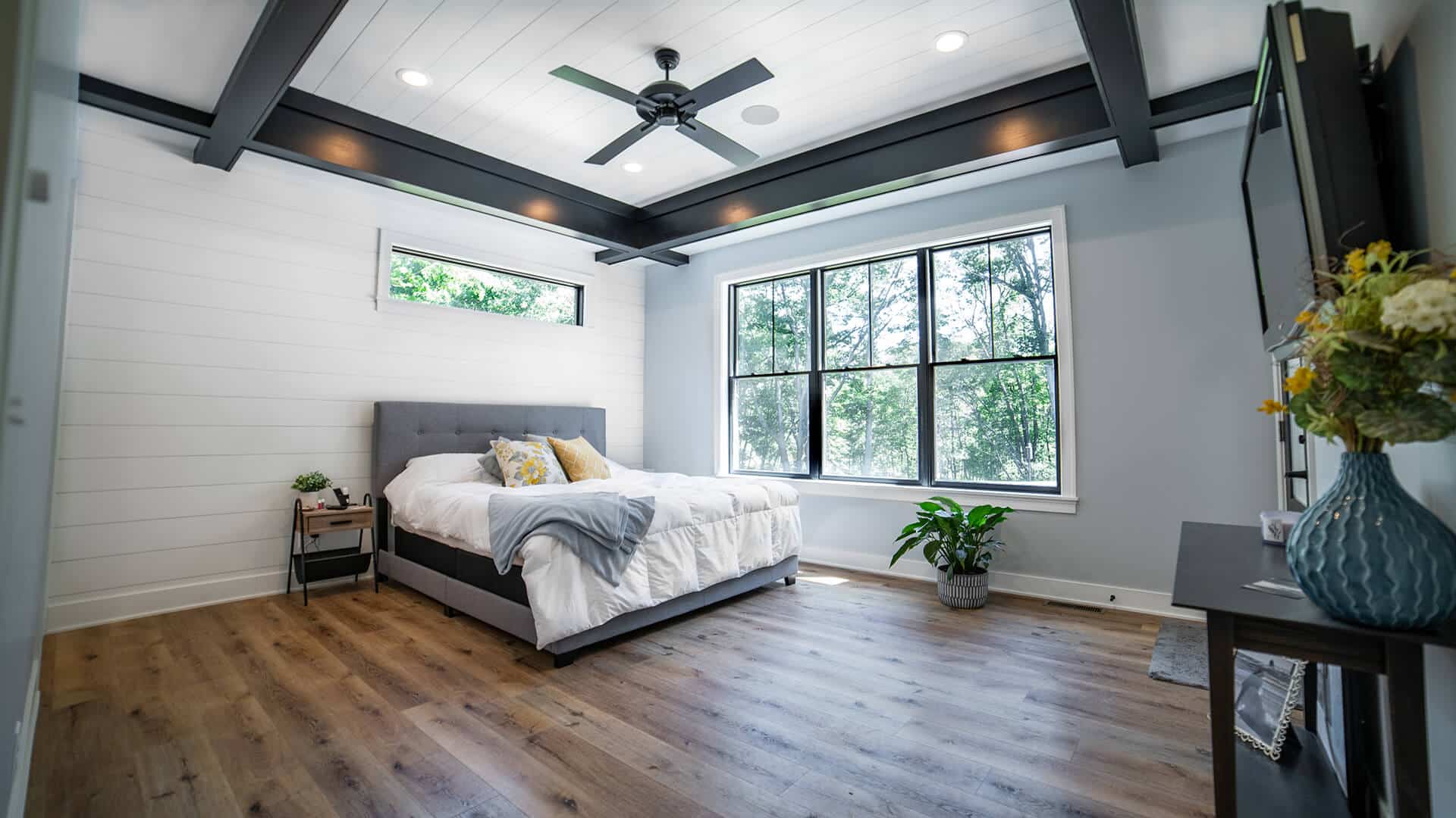 Bedroom with large windows, modern ceiling beams, and cozy decor.