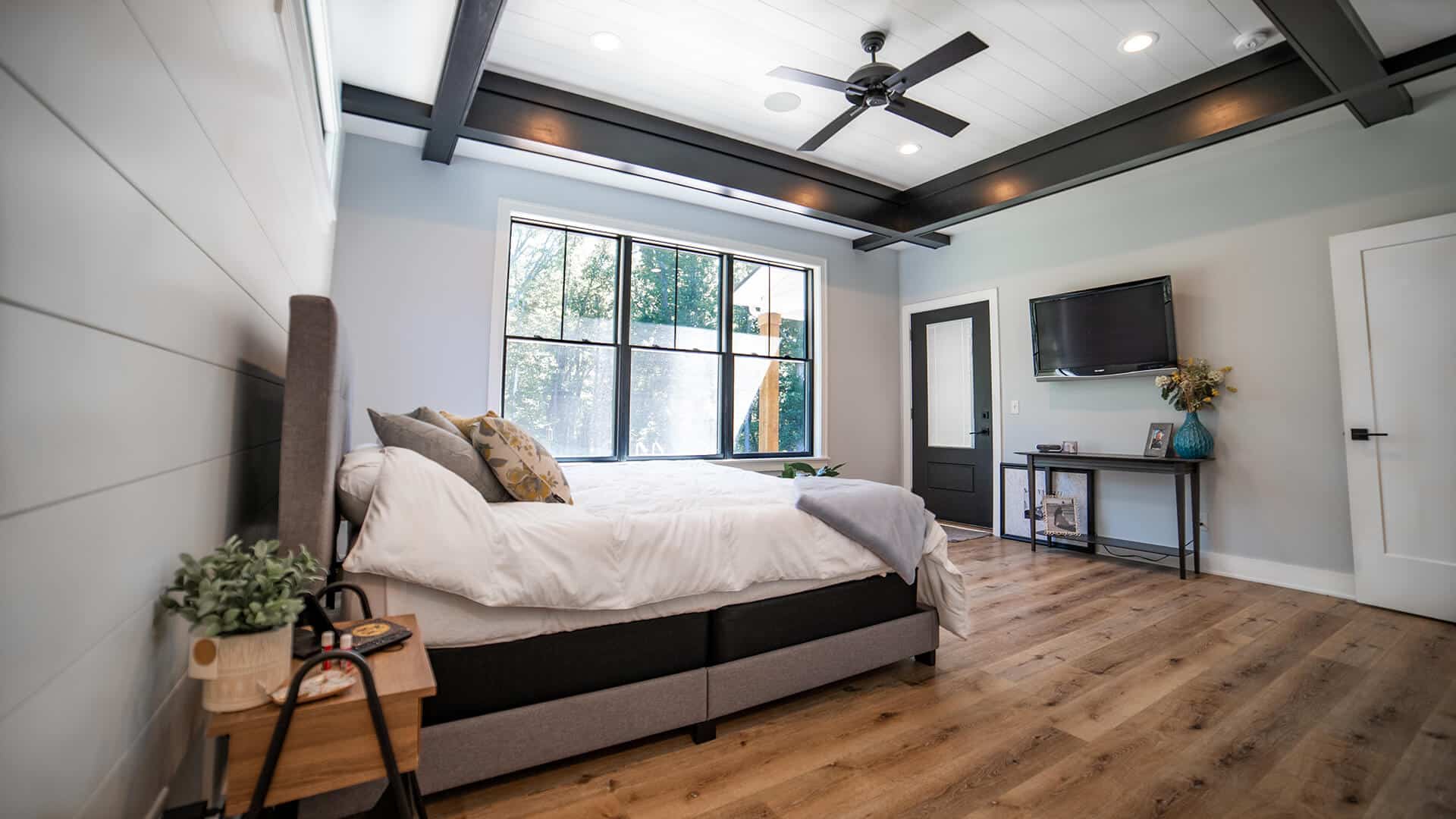 Bedroom with large window, modern ceiling fan, and cozy furnishings.