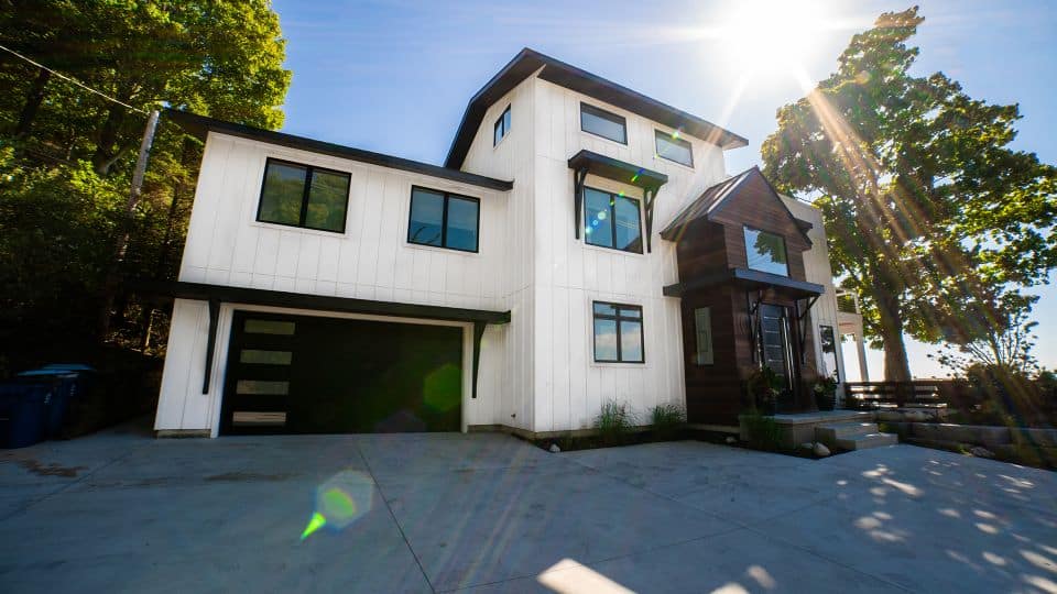 Contemporary white house with black accents and large windows in a lush green setting.