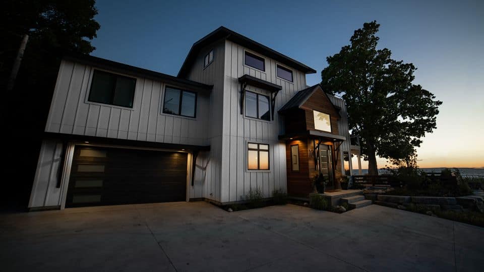 Modern white house with a spacious garage, surrounded by trees, at sunset. Perfect for families seek.