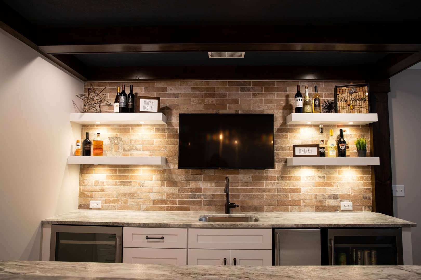 Living room with brick accent wall, mounted TV, and stylish shelves with decor and bottles.