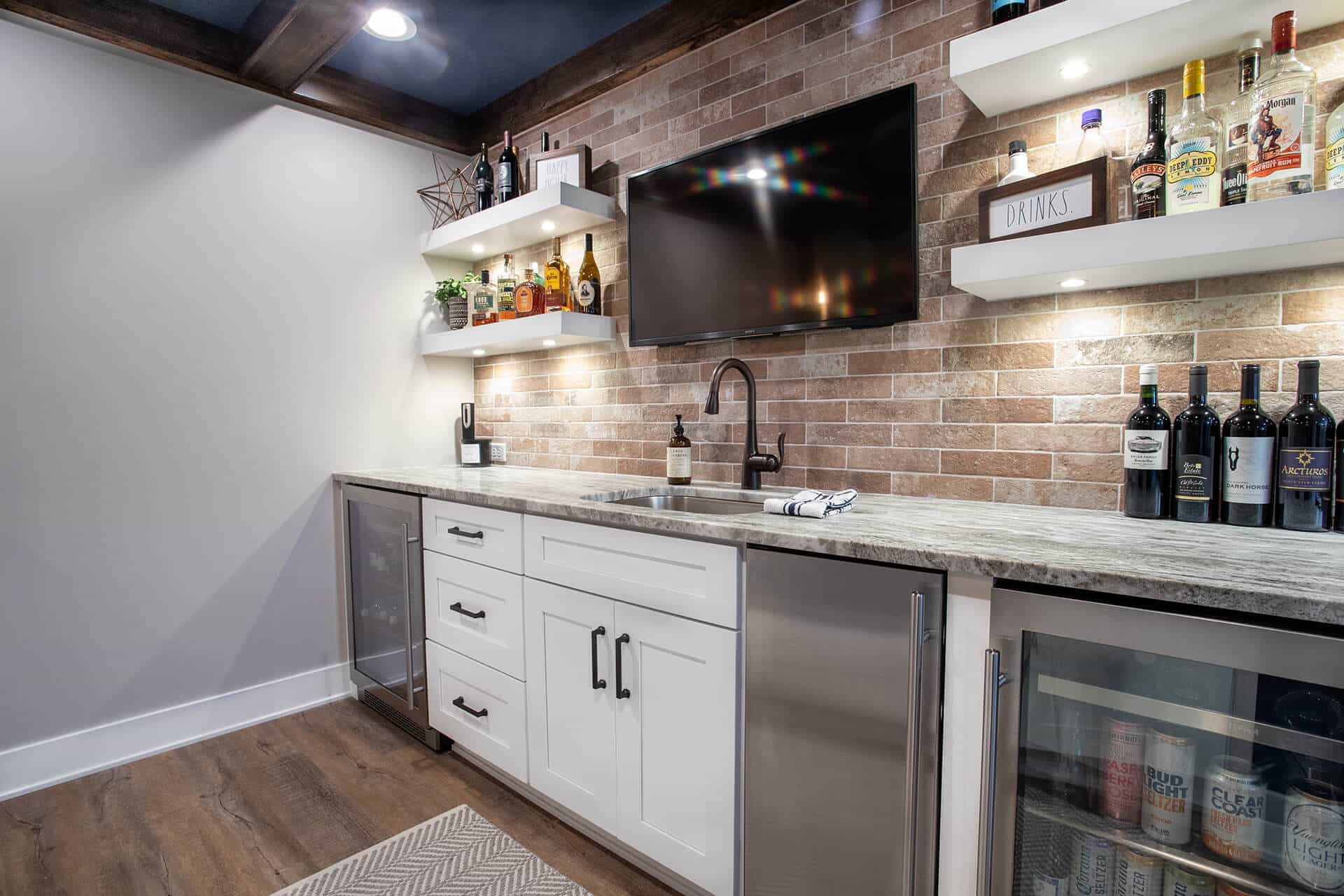 Modern home bar with brick wall, white cabinets, and liquor shelves.