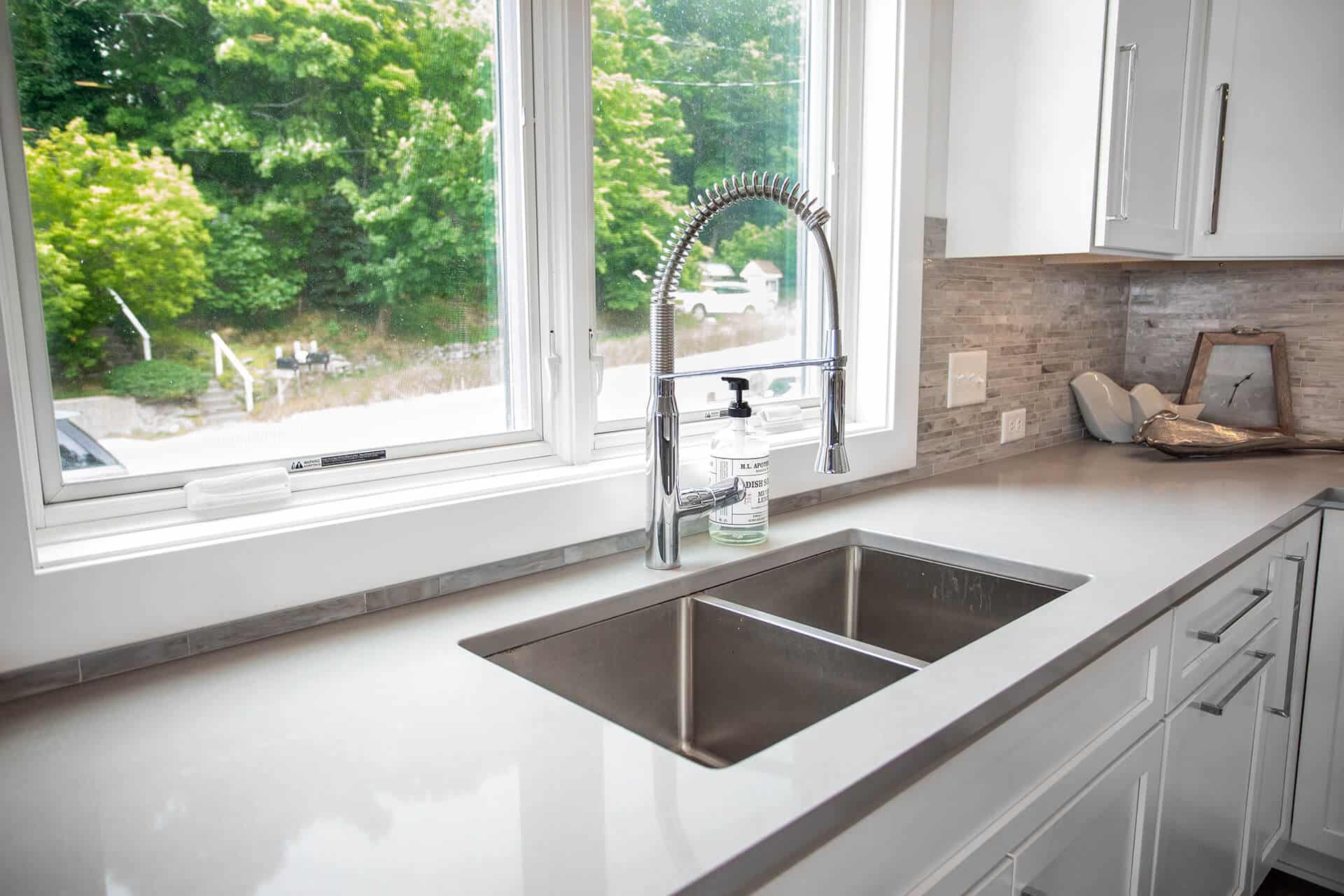 Modern kitchen sink with stainless steel basin and view of lush trees through window.