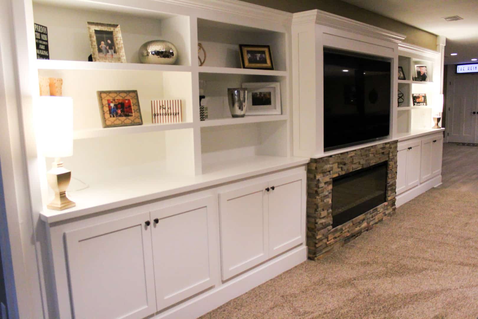 Modern white built-in entertainment center with fireplace and shelving.