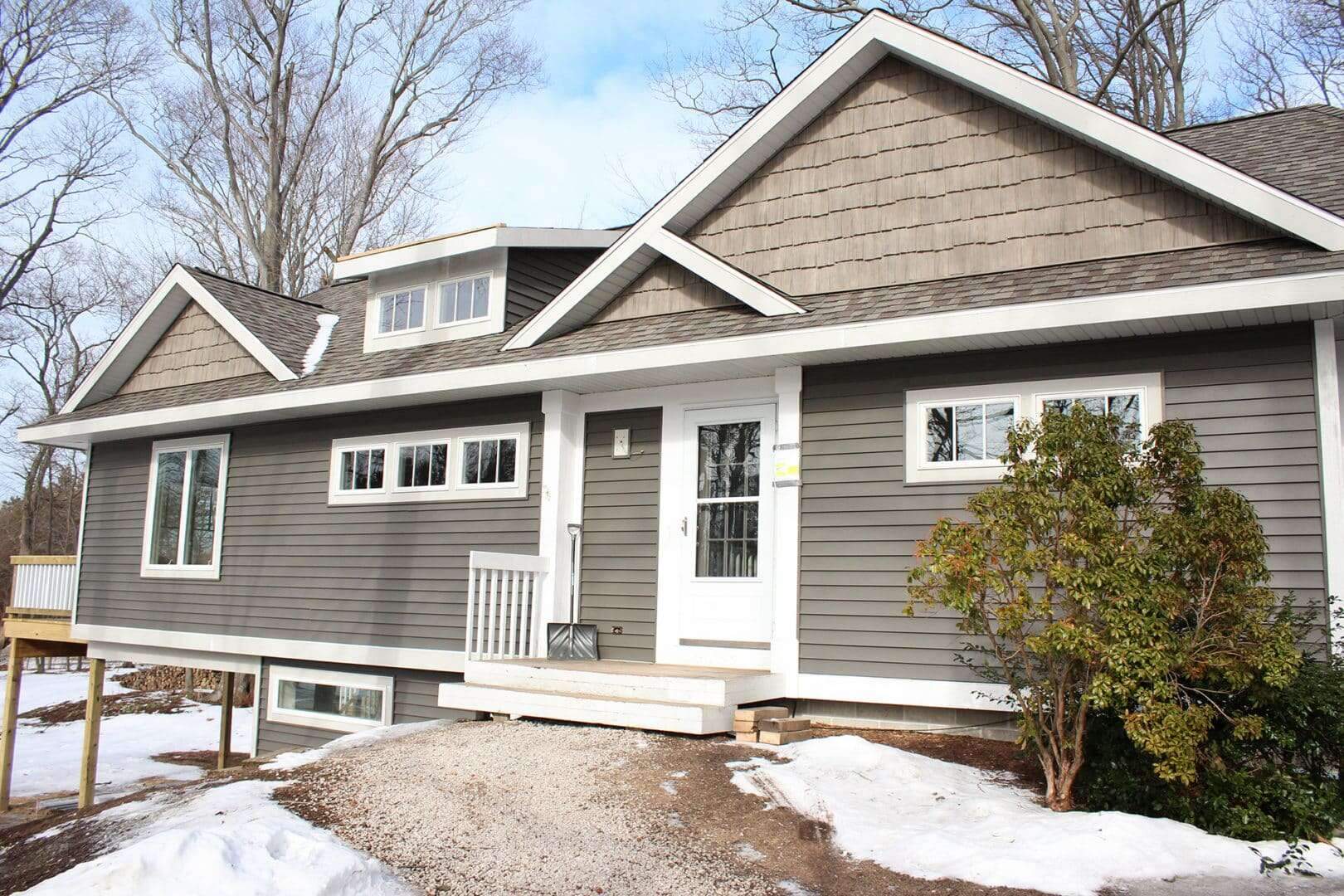Beautiful gray residential home with white accents, surrounded by snow and trees.