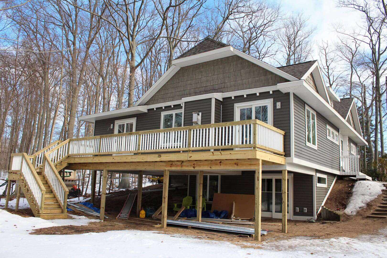 Modern gray house with spacious elevated deck in a wooded setting.